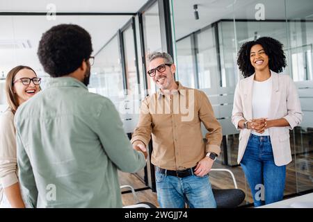 A friendly office environment is depicted where a team greets each other, shaking hands, showcasing the warmth and positive relationships between colleagues in a modern business setting. Stock Photo