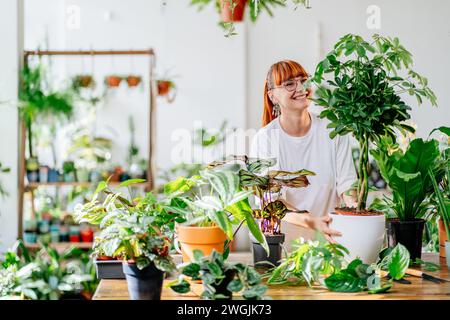 Small business. Smiling positive florist red haired young woman in glasses holding a plant at pot. Stock Photo