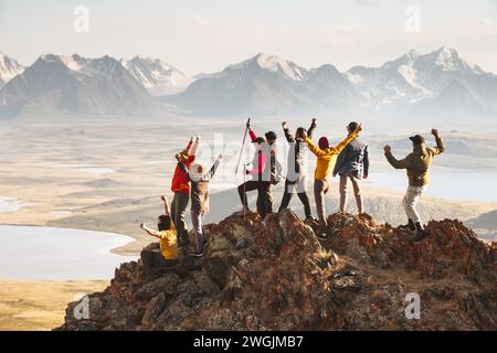 A large group of diverse tourists celebrates the completion of their climb to the top of the mountain with great view at sunset. Mixed ages and skills Stock Photo