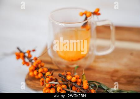Cup with fragrant vitamin tea from sea buckthorn on a wooden table. Fresh sea buckthorn berries on a branch are ready for the preparation of a healing Stock Photo