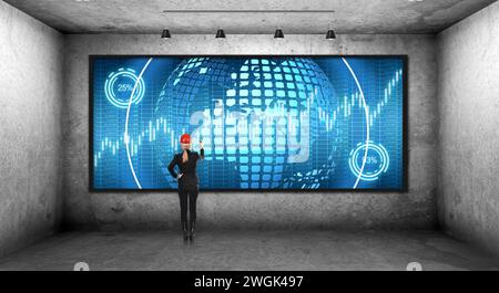 Businesswoman in a helmet draws a business hologram on digital screen. Concrete dark room. Virtual reality and global networking concept. Stock Photo