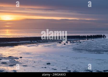 Old breakwater exposed during low tide on the Wadden Sea at sunset. It is low tide, causing much of the Wadden Sea (UNESCO) to be mostly dry. Stock Photo