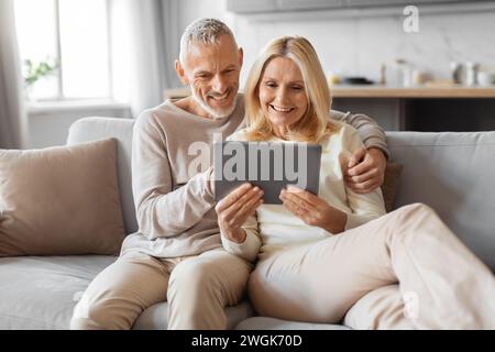 Positive retired couple using digital tablet at home Stock Photo