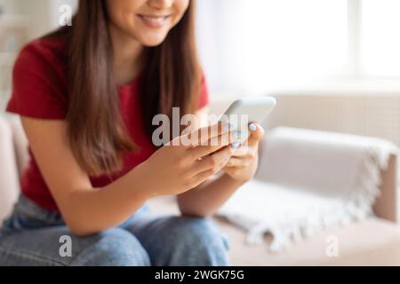 Young asian woman focused on her smartphone sitting on couch at home Stock Photo