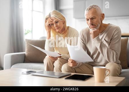 Senior Couple Checking Financial Documents, Sitting On Couch At Home Stock Photo