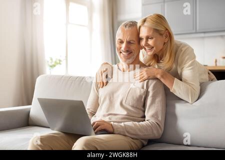 Positive beautiful loving senior spouses using laptop at home Stock Photo
