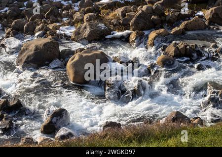 Detail of the bottom of the waterfall. Stones and rock and flowing water, partly frozen into big pieces of ice. Autumn in north-east Iceland, Rjukanda Stock Photo