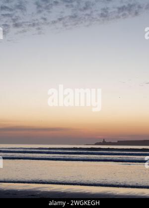 Waves roll in at sunset with an Island on the horizon in Essaouira, Morocco, 5th Feb 2024 Stock Photo