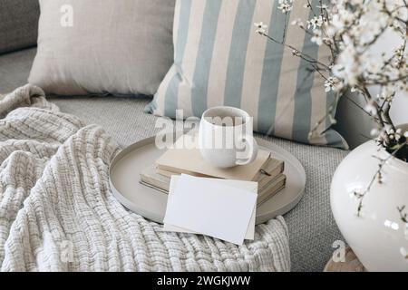 Spring breakfast scene. Blank greeting card mockup. Cup of coffee, tea on books. Round beige tray. Blossoming cherry plum tree branches in ceramic Stock Photo