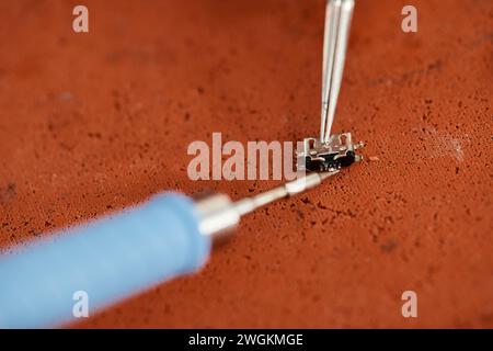 close up view of soldering iron and tweezers near electronic chipset on table in repair workshop Stock Photo