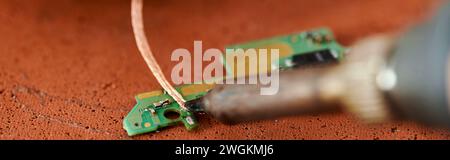 soldering iron near microscheme of electronic device on table in repair workshop, horizontal banner Stock Photo