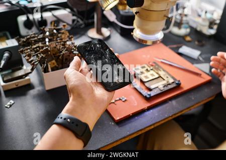 cropped view of repairman holding smartphone with broken screen near electronic tools in workshop Stock Photo