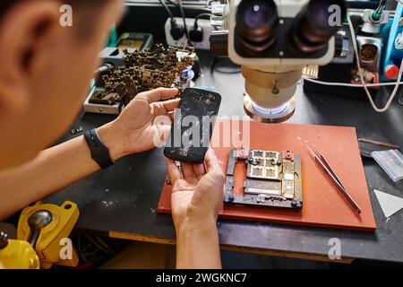 cropped view of experienced technician holding mobile phone with broken screen near repair equipment Stock Photo