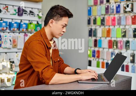 concentrated asian man using laptop on counter in private electronics shop, small business concept Stock Photo