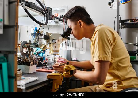 side view of professional asian specialist with microscope examining electronic device in workshop Stock Photo