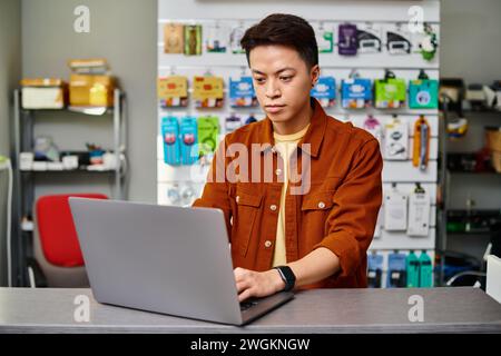 serious asian man using laptop on counter in private electronics store, small business concept Stock Photo