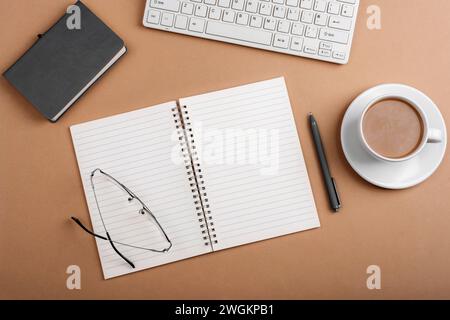 Desktop with blank notepad, keyboard, glasses and coffee cup on brown table. Top view, flat lay. Stock Photo
