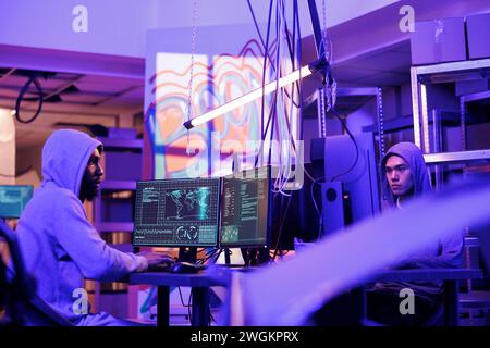 Hackers breaking website and cracking password while doing illegal activity. Criminals breaching security system and stealing valuable information in hideout workspace at night Stock Photo