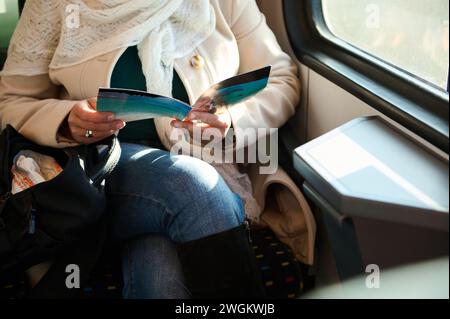 Close-up a leaflet in the hands of a female commuter passenger riding on a high speed train. people. Leisure. Rail road transportation Stock Photo