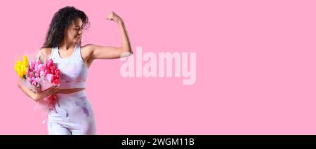 Young sporty African-American woman with bouquets of flowers showing muscles on pink background with space for text. International Women's Day celebra Stock Photo