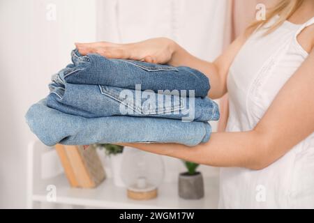 Young woman with stack of stylish jeans in wardrobe at home, closeup Stock Photo