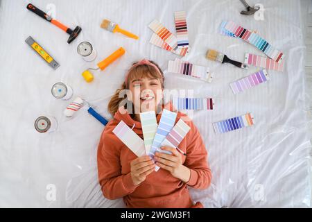 Young woman with color palettes and paint tools lying on bed, top view Stock Photo