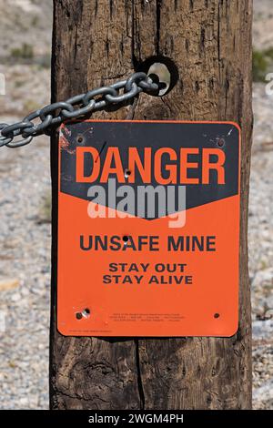 orange and black danger unsafe mine sign on a wood post with a few bullet holes Stock Photo