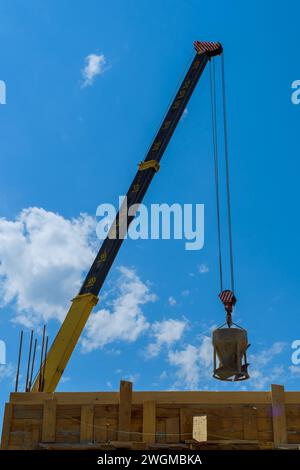 At construction site, tower crane lifts bucket of concrete cement mix for pouring into formwork Stock Photo