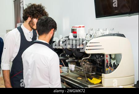 Baku, Azerbaijan, January 12, 2019: Preparing coffee for a client. Handsome young man in apron making coffee at the coffee machine while standing at Stock Photo