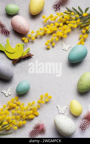 Decorative Easter composition featuring pastel-colored eggs, vibrant mimosa branches, and festive cutouts on a light, textured surface. Stock Photo