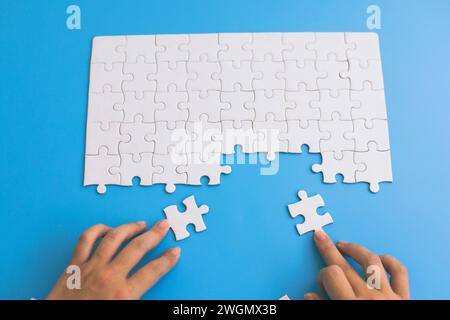 Hand put the last piece of jigsaw puzzle to complete the mission. Concept of connecting jigsaw pieces, problem solving, teamwork and success. Stock Photo