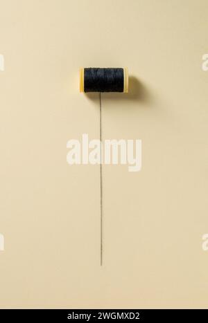 Black sewing thread wrapped around a partially unwrapped plastic spool on a yellow background Stock Photo