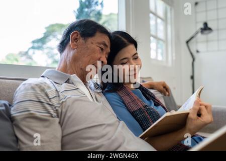 Retired elderly couple sits on couch in their home reading relaxing book. Senior Activity Concept Stock Photo