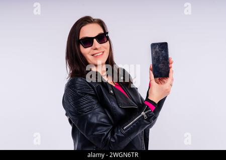 A frustrated young woman with a broken phone in her hands. White isolated background. Broken Gadget Stock Photo