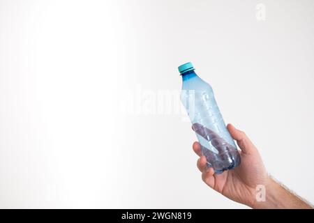 Light blue, empty, transparent plastic bottle held by Caucasian male hand, isolated on white Stock Photo