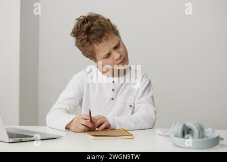 Smiling boy using laptop for elearning at home, enjoying online education and playing educational games He sits at a table, surrounded by books and Stock Photo