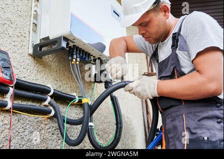 Man electrician installing solar panel system. Technician in helmet and gloves making electrical wiring inverter and electric box. Concept of alternative and renewable energy. Stock Photo
