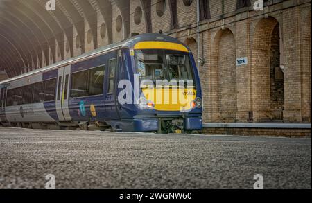 A low angle view of a locomotive waiting at railway station platform. A brick wall with circular windows is behind. Stock Photo