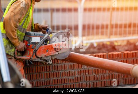 Groundworker builder cutting plastic foul drainage pipe using a petrol-powered saw close-up Stock Photo