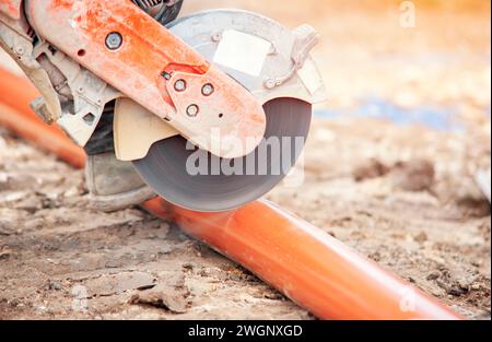 Groundworker builder cutting plastic foul drainage pipe using a petrol-powered saw close-up Stock Photo