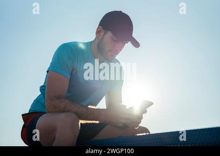 A man in a hat using cell phone, sitting on a bench Stock Photo