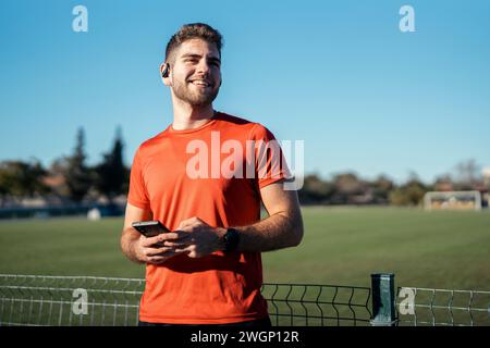 A young man in a vibrant orange shirt confidently stands in a sunlit field Stock Photo