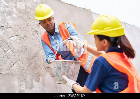 Female bricklayers holding bucket against wall Stock Photo