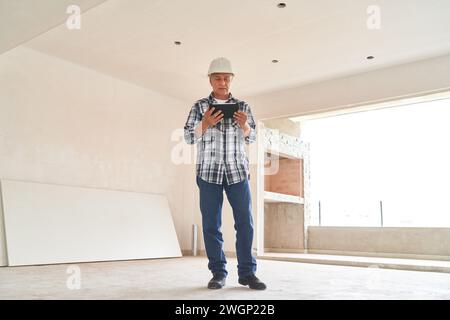 Contractor wearing hardhat standing with tablet PC Stock Photo