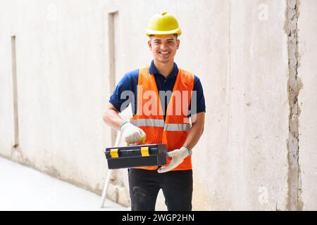 Smiling male construction worker holding toolbox Stock Photo