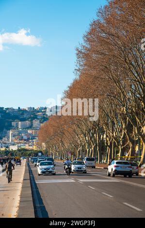 Naples, Italy - December, 18, 2022: A bustling street in Naples, Italy, filled with vibrant people and cars driving along the picturesque Caracciolo w Stock Photo