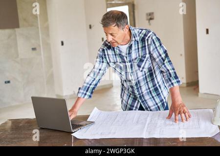 Senior architect using laptop by blueprint at desk Stock Photo