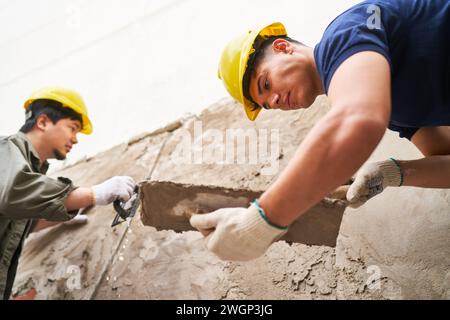Young male masons using trowels for plastering wall Stock Photo