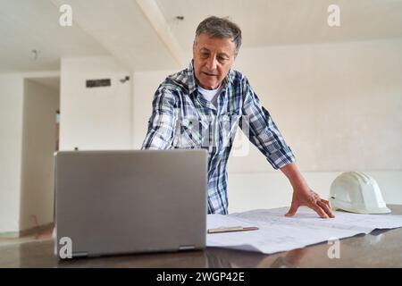 Senior architect using laptop by blueprint at desk Stock Photo