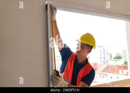 Young carpenter measuring window frame with tape Stock Photo